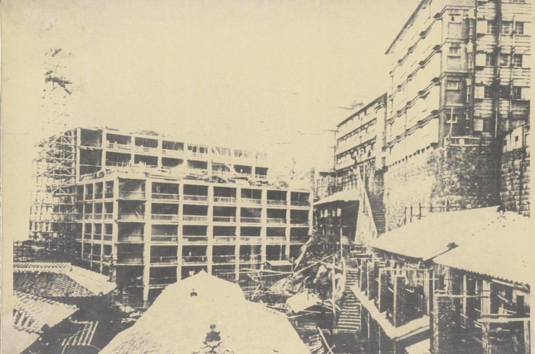 正面は労働者用の日給社宅17号棟、6階建鉄筋コンクリート造。奥の建物は16号棟で、9階建へ増築工事中の写真である。当初の計画では、更に3層を増築し12階建てになる予定だった。コンクリートや資材昇降用足場が確認できることから、1918（大正７）年の写真である。右側手前の建物は、大正2（1913）年建設の木造5階建て鉱員社宅。屋上庭園を設け、各階の床はコンクリートだった。